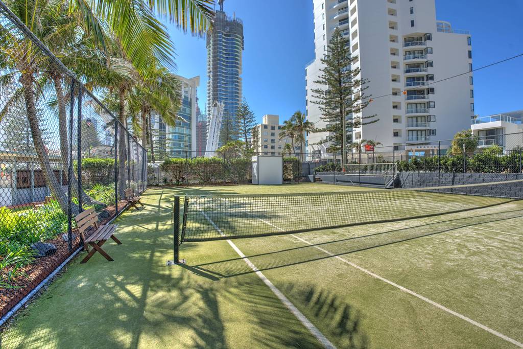 Tennis court with net posts, palm trees and surrounding highrise apartment buildings